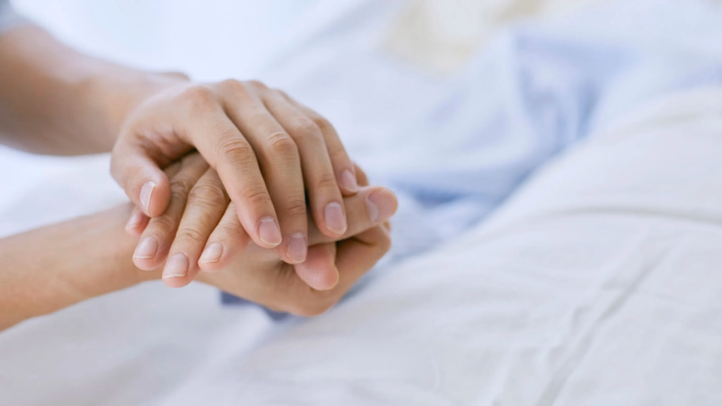 Two hands holding each other on a medical bed for support.